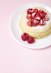 A stack of berry covered pancakes on a pastel pink background with blank space below