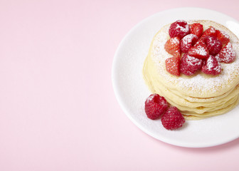 A stack of berry covered pancakes on a pastel pink background with blank space at side