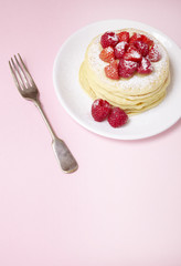A stack of berry covered pancakes on a pastel pink background with fork and blank space below