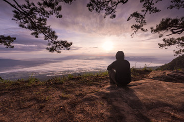 Young man sitting alone outdoor on cliff with beautiful sunrise view from the top. .
