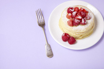 A stack of fruit covered pancakes on a pastel purple background with fork and blank space at side