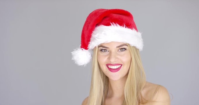 Adorable beautiful girl posing isolated in Santa Claus Hat on gray backround. She smiling to the camera. Bare shoulders.