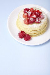 A stack of berry covered pancakes on a pastel blue background with blank space below