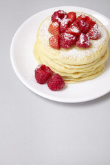 A stack of berry covered pancakes on a soft grey background with blank space below