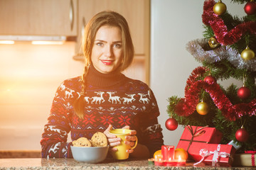 Young happy woman holding cup of tea close to the Christmas tree