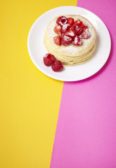 A stack of fruit covered pancakes on a pink and yellow background forming a page header