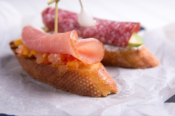 Bruschetta crostini with salami, avocado and ricotta cheese on a slate plate, parchment, on a white table. Italian cuisine
