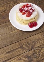 A stack of fruit covered pancakes on a wooden breakfast table background