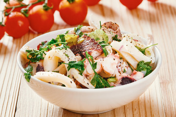 Seafood salad in white bowl, cherry tomato in the background