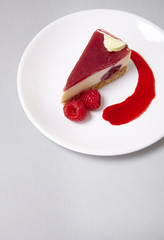 A slice of raspberry cheesecake dessert on a soft grey background forming a page header