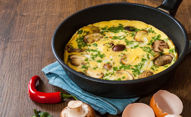 omelette with mushrooms in a frying pan on wooden table