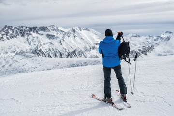 Skier standing on mountain peak and preparing to go down the slope.