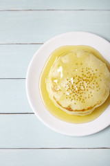 Overhead view of a stack of golden syrup covered pancakes on a blue wooden background