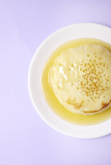 Aerial view of a stack of hotcakes with golden syrup on a pastel purple background