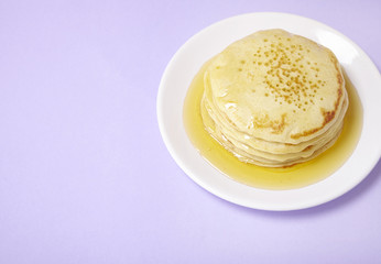 A stack of hotcakes with golden syrup on a pastel purple background forming a page border