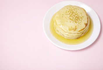 A stack of pancakes with golden syrup on a pastel pink background forming a page border