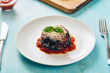 Parmigiana di melanzane - Eggplant parmesan on white dish and blue table