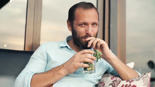 Happy man talking to camera and drinking cocktail in cafe
