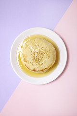 A stack of pancakes with golden syrup on a pastel pink and purple background