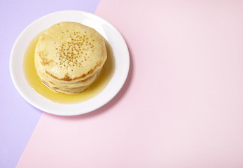 A stack of flapjacks with golden syrup on a pastel pink and purple background 