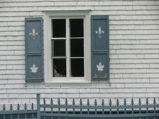 fenêtre dont les volets sont découpés des symboles du Québec et du Canada.