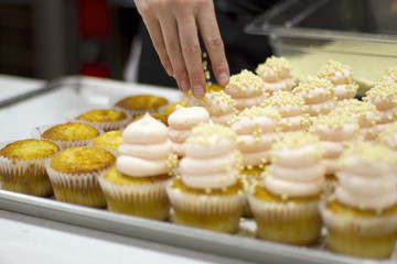 Baker Decorating Cupcakes with Pink Frosting with Nonpareil Candy