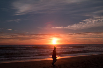 Fototapeta na wymiar A woman walks on the beach at sunset.