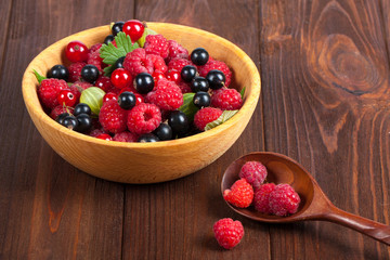 Fresh ripe berries in a wooden plate on the old wooden table. Useful natural food. Fruits and berries