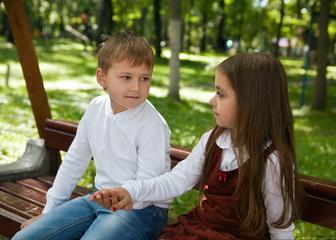 A girl with a boy holding hands, sitting on a bench in the Park