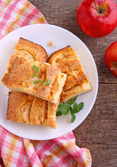 homemade pie with apples and cinnamon is cut slices on a plate, wooden background