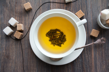 White porcelain cup with green tea and sugar cubes on wooden table. Top view.