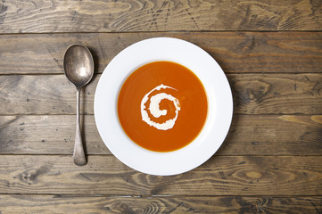 Aerial view of a bowl of hot tomato soup with swirl of cream and spoon on a reclaimed table background