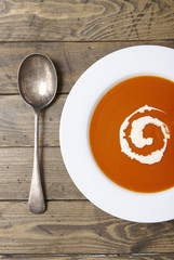 Aerial view of a bowl of hot tomato soup with swirl of cream and spoon on a wooden table top