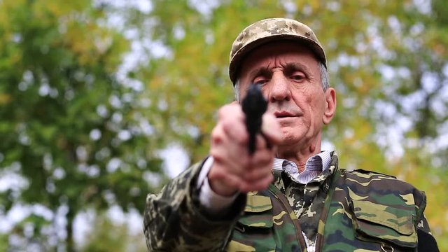 Man with gun. Man with black revolver in hand looks at the camera. Retired officer in military uniform at shooting range. Man holds in hands black revolver
