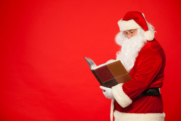 Santa Claus reads old book, on a red background. Christmas