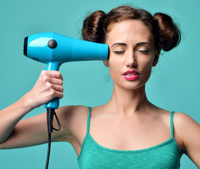 Happy young curly brunette woman with hair dryer on blue mint ba