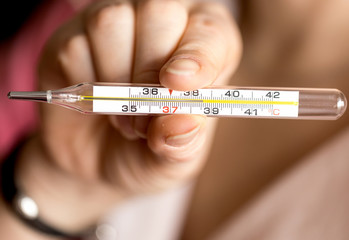 Female hand holding a medical thermometer with high temperature.