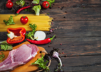 Italian food background, with meat, tomatoes, spaghetti, garlic, peppercorns, chili pepper on wood table