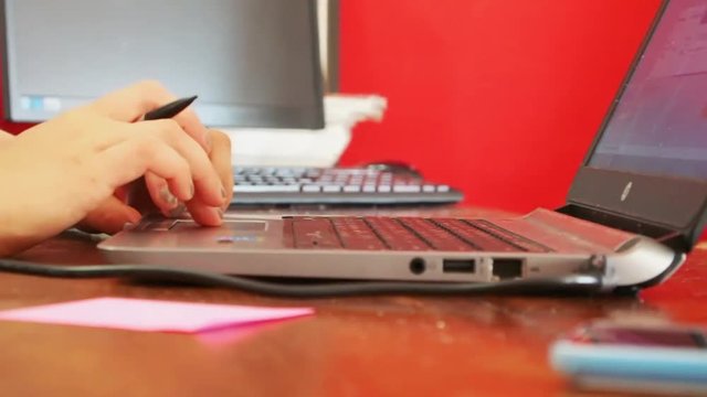 Femaile Fingers With Nice Manicure With Grey Nails Are Touching Touchpad of a Laptop and Holding a Pen, Red Background, Close up
