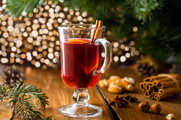 Fototapeta na wymiar Glass of mulled wine by Christmas tree. Traditional delicious drink for New Year party