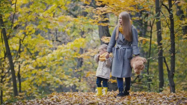 Little daughter with her mother and Teddy Bear walking in autumn park