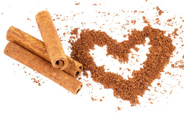 Cinnamon sticks and cacao powder in shape of heart, isolated on white background.