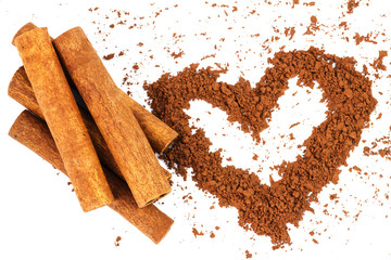 Cinnamon sticks and cacao powder in shape of heart, isolated on white background.