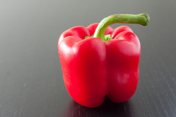 A single ripe red bell pepper on a dark wooden background