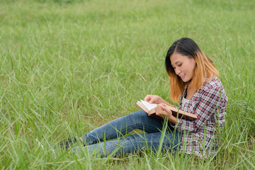 Young woman reading book on meadows field.