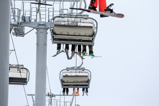 Legs of ski and snowboard riders on a cable chair lift in cloudy snowy winter mountains scenic close up