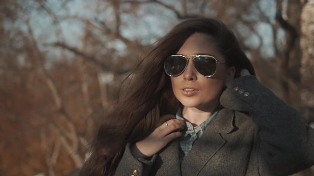 Woman in coat and sunglasses in autumn park. Student girl walking in glasses and posing.