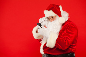 Photo of Santa Claus using mobile phone, on a red background. Christmas