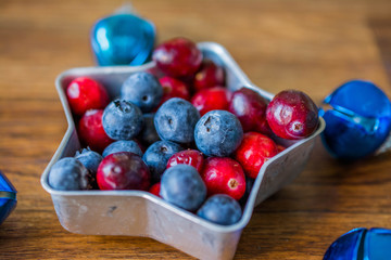 Cranberries and blueberries on plate in the form of stars. Blue Christmas balls on the Christmas tree
