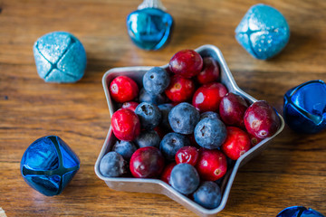 Cranberries and blueberries on plate in the form of stars. Blue Christmas balls on the Christmas tree